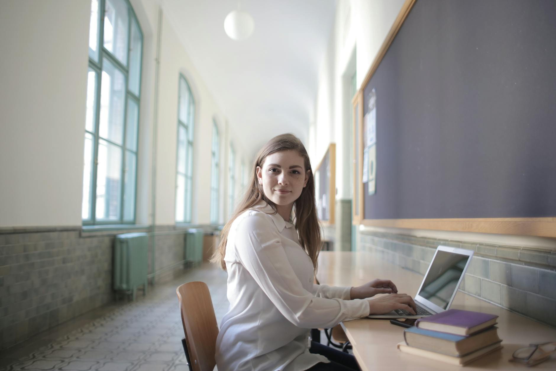 female student typing on laptop in university hallway